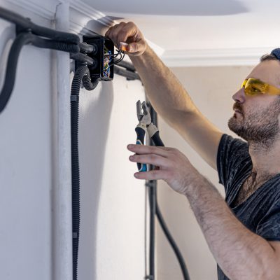 An electrician is mounting electric sockets on the white wall indoors.