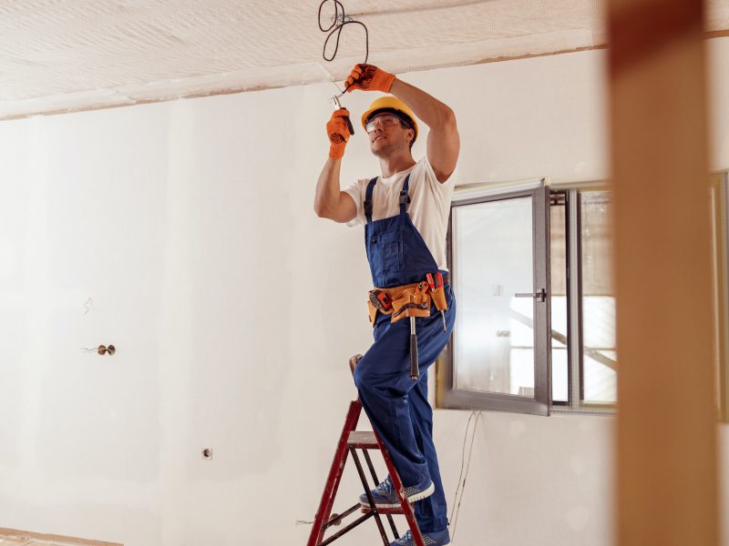 Smiling electrician fixing electric cable on ceiling